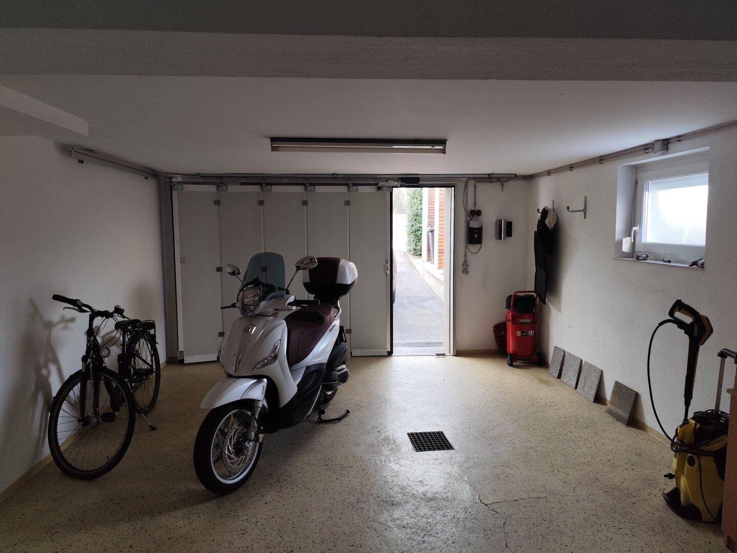 Geräumige Garage mit Platz für Motorrad und Fahrräder, inklusive Fenster.