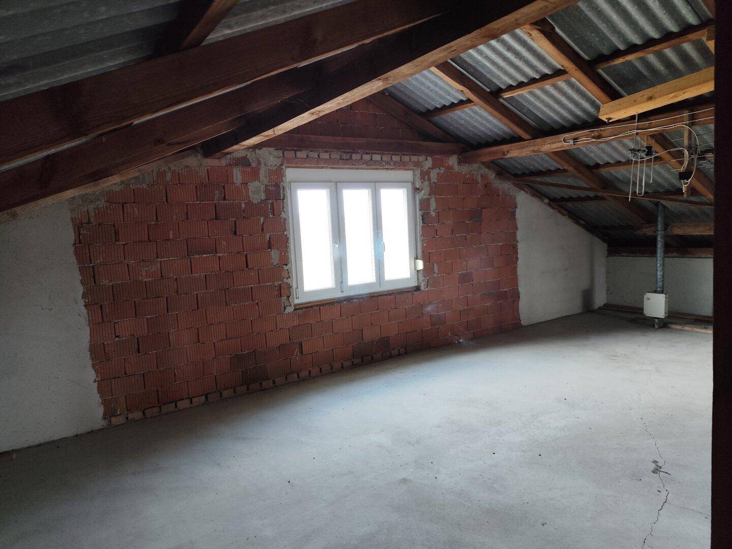 Unausgebauter Dachboden mit sichtbaren Ziegelwänden und Dachbalken, bietet Ausbaupotenzial.