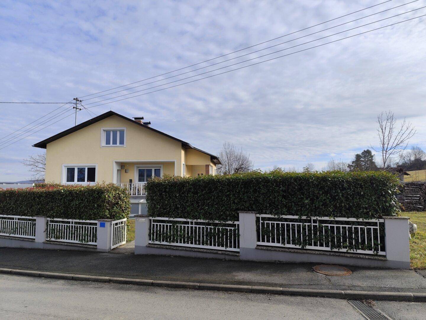 Ansicht des Hauses von der Straße mit gepflegter Hecke und Zaun im Vordergrund.