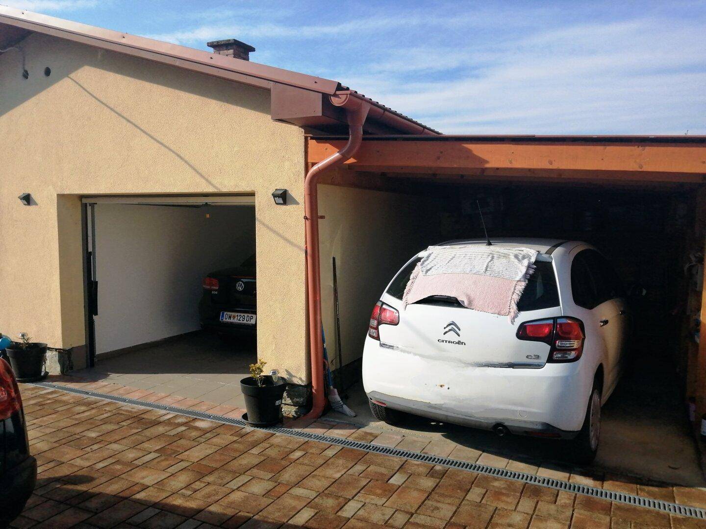 Doppelgarage mit gepflasterter Zufahrt, ein Auto parkt innen, ein weiteres in der offenen Bucht.