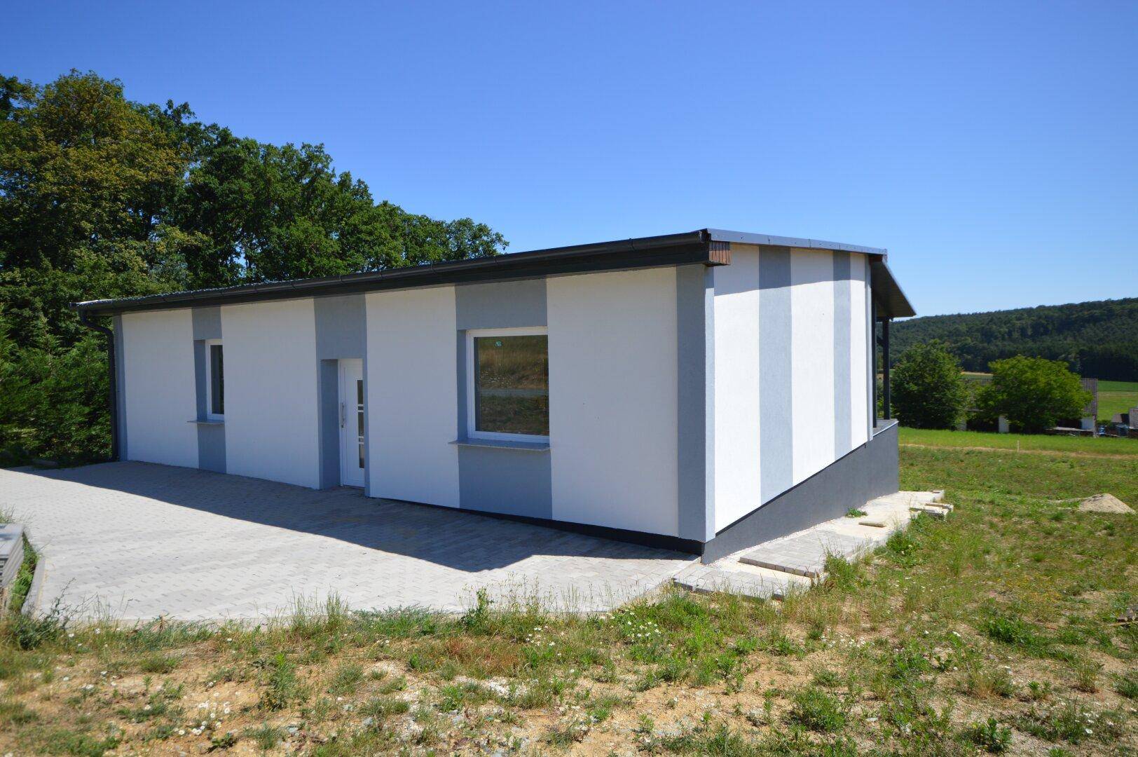 Moderne Fassade des Neubaus mit gepflasterter Zufahrt und weitem Blick in die Landschaft.