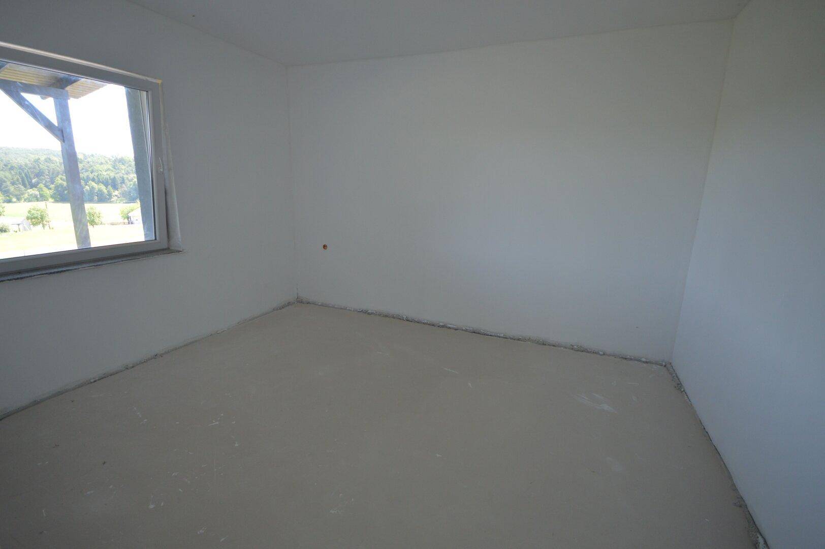 Unfertiges Schlafzimmer mit Fenster, das viel Tageslicht hereinlässt und eine grüne Aussicht bietet.