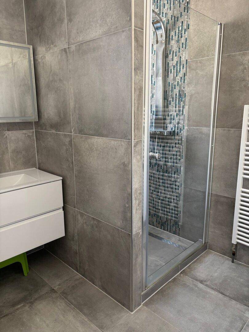 Modernes Badezimmer mit grauen Fliesen, Duschkabine aus Glas und beheiztem Handtuchhalter.