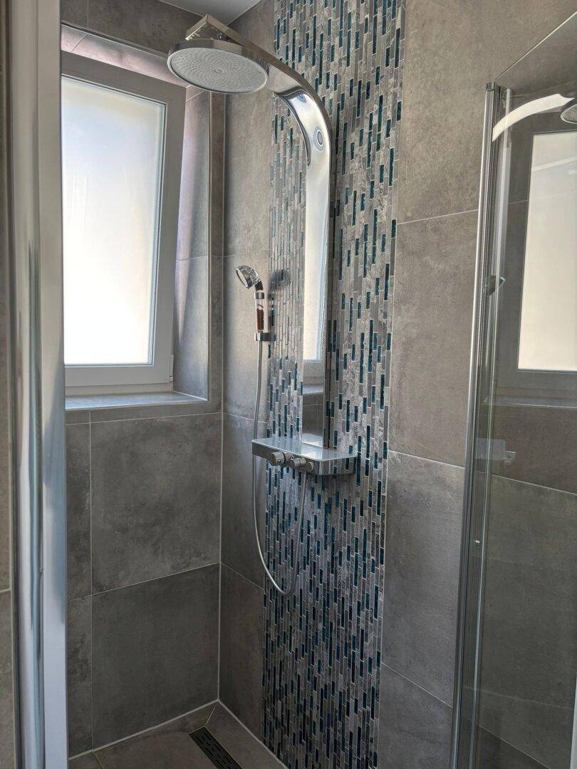 Duschbereich im modernen Badezimmer mit Regendusche und dekorativen Mosaikfliesen.