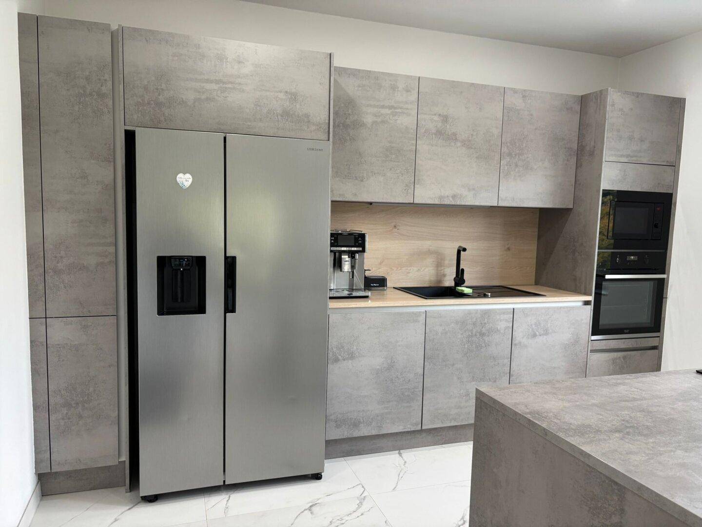 Moderne Küche mit grauen Schränken, großem Kühlschrank und integrierten Elektrogeräten.