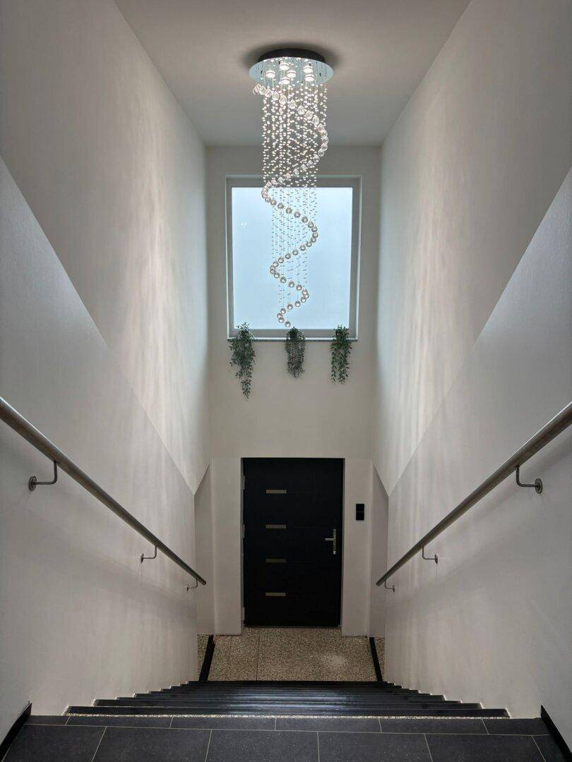 Treppenhaus mit dunklen Stufen, elegantem Kronleuchter und Fenster für natürliches Licht.
