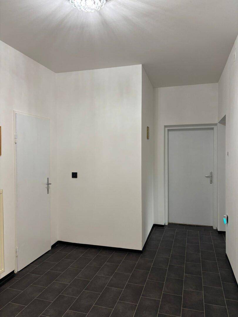 Geräumiger Flur mit dunklem Fliesenboden und schlichten weißen Wänden.