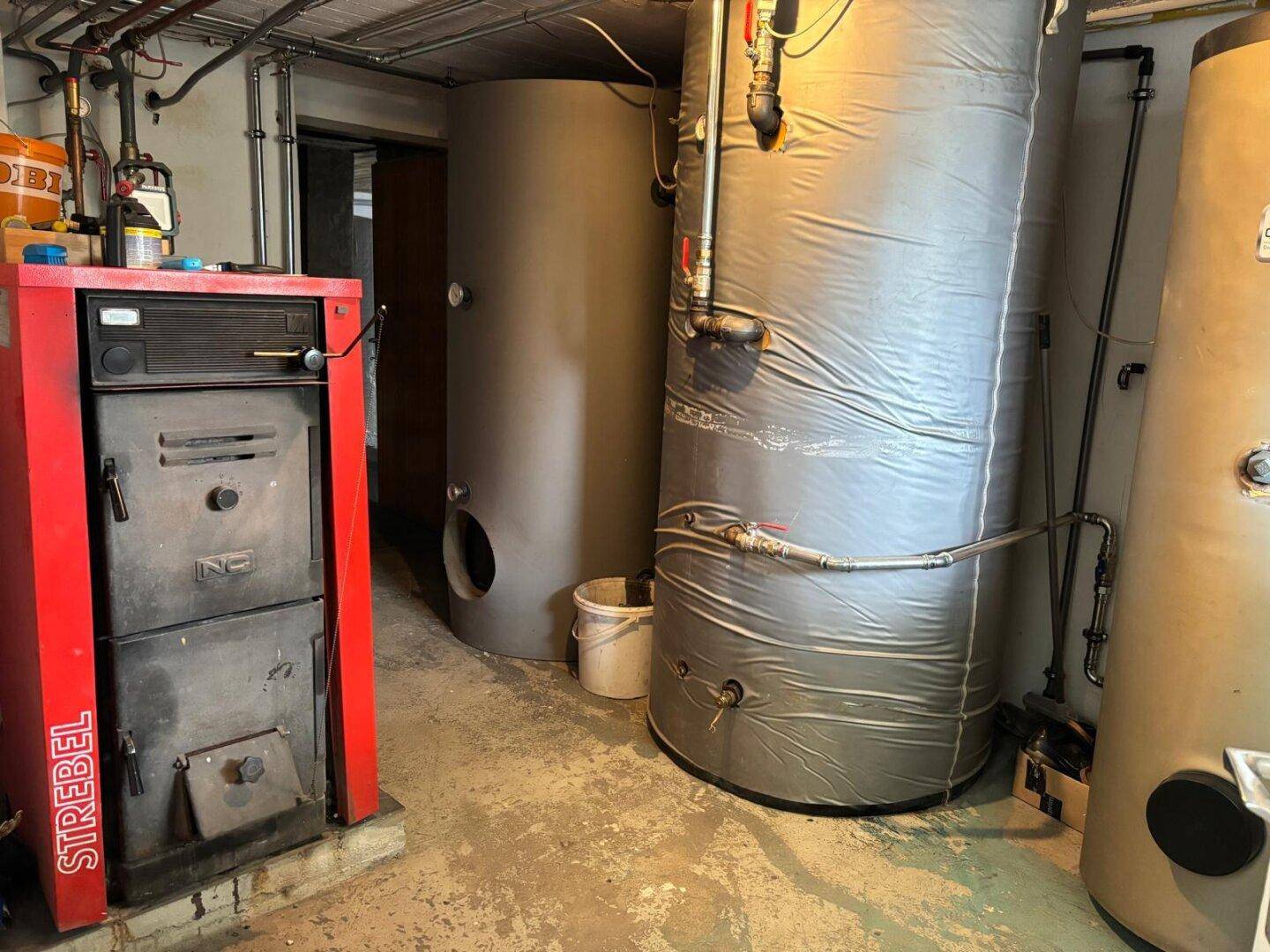 Heizungsraum im Keller mit einem roten Ofen und großen Warmwasserspeichern.