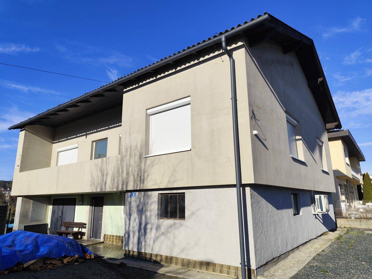 Seitenansicht des Hauses mit Balkon, Rollläden und Klimaanlage unter blauem Himmel.