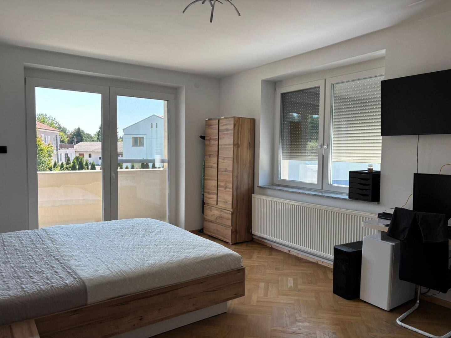 Schlafzimmer mit Holzboden, Zugang zum Balkon und viel natürlichem Licht durch große Fenster.