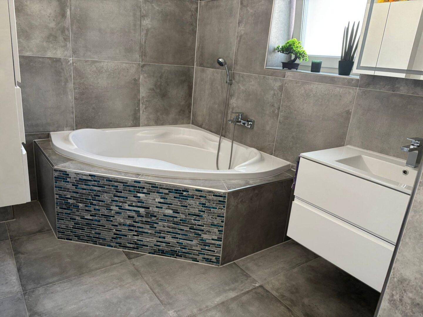 Modernes Badezimmer mit grauen Fliesen, Eckbadewanne und stilvollem Waschtisch.