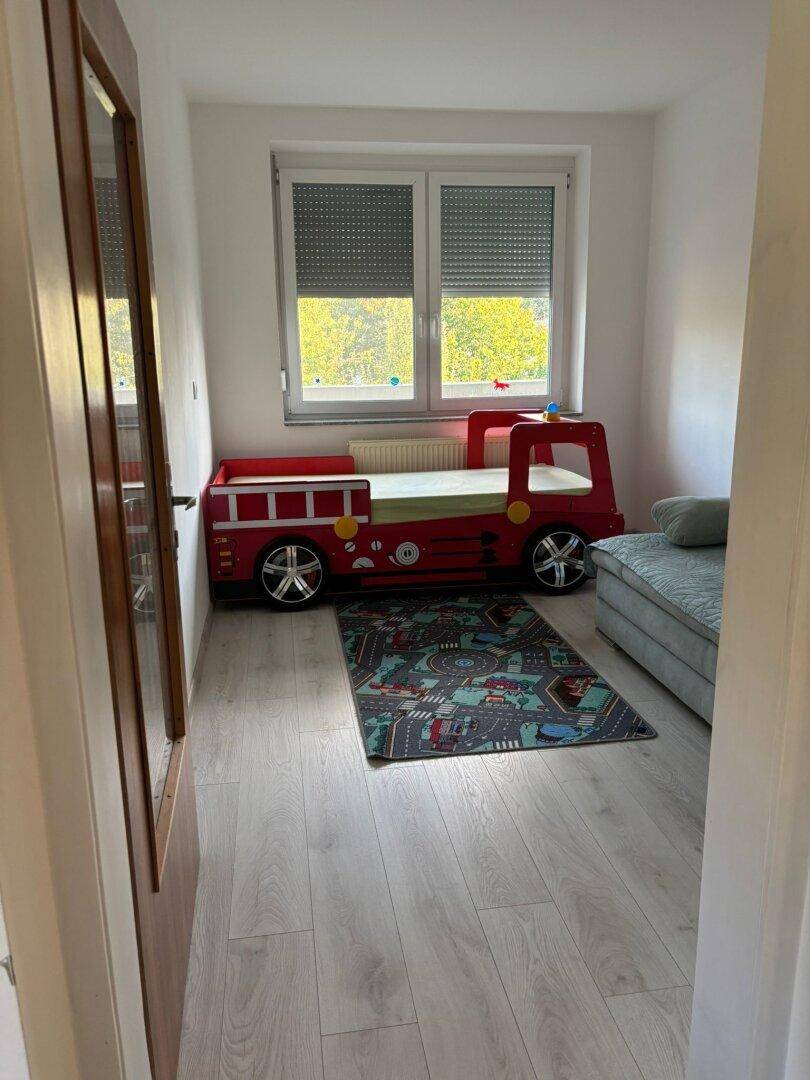 Kinderzimmer mit einem einzigartigen Feuerwehrauto-Bett und hellem Laminatboden.