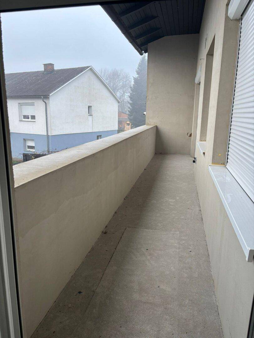 Langer, schmaler Balkon mit Betonboden und hohen Brüstungswänden.