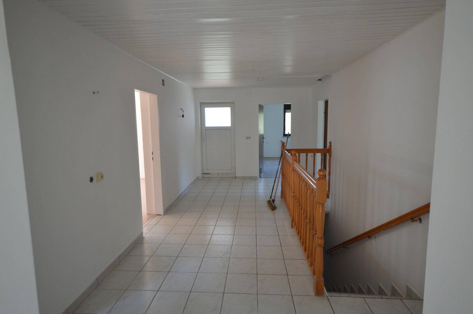 Heller Flur mit weißen Fliesen, Holztreppe und Zugang zu weiteren Räumen.