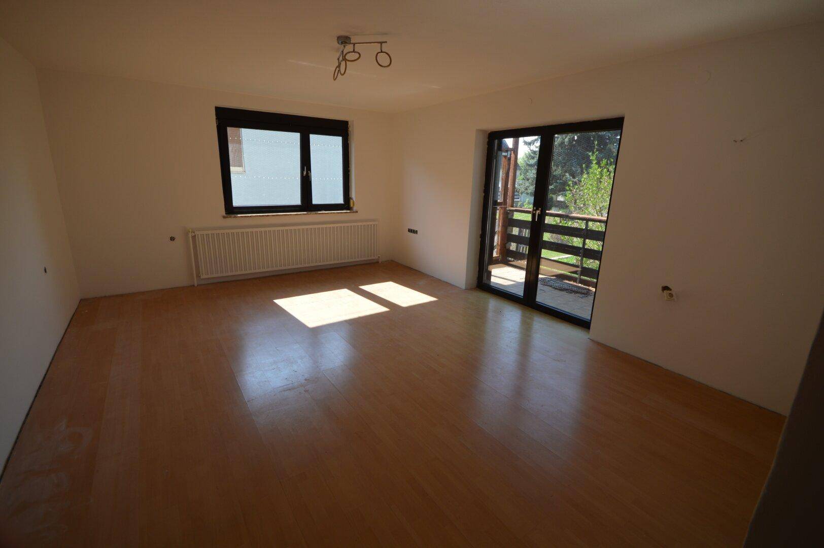 Heller Wohnraum mit Laminatboden, großem Fenster und direktem Zugang zum Balkon.
