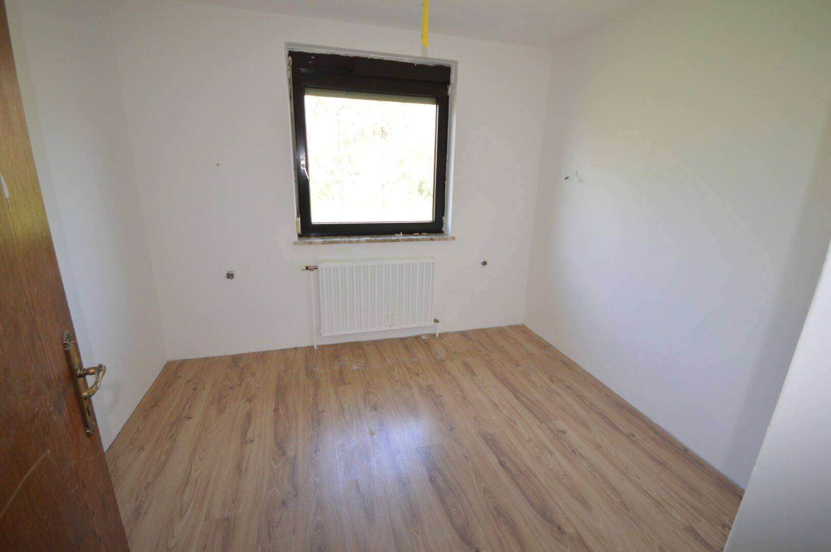 Helles Zimmer mit Laminatboden und einem Fenster, ideal als Kinder- oder Gästezimmer.