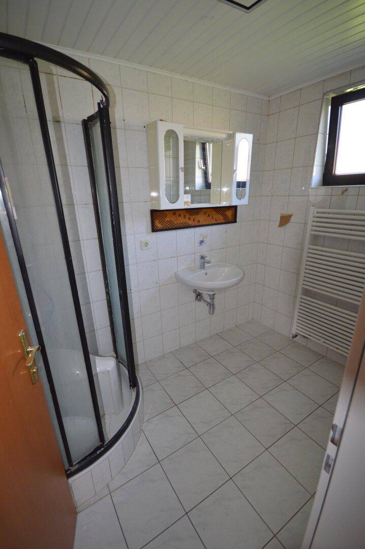 Badezimmer mit Duschkabine, Waschbecken, Spiegelschrank und einem Fenster für Tageslicht.