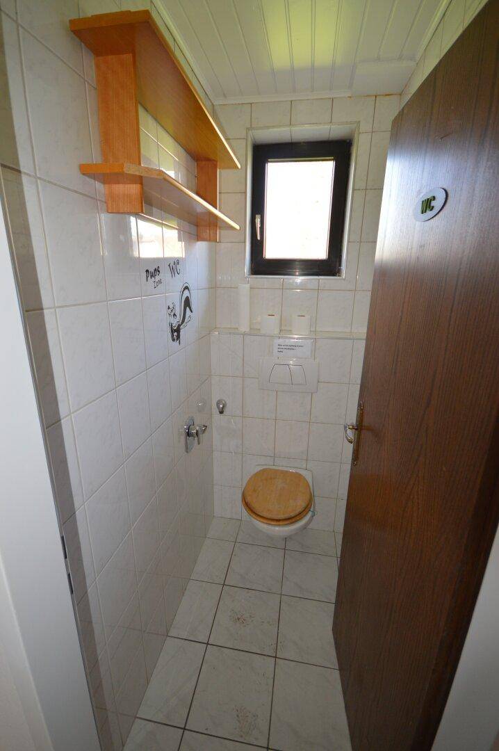 Separates WC mit Toilette, kleinem Waschbecken und einem Fenster für Belüftung.