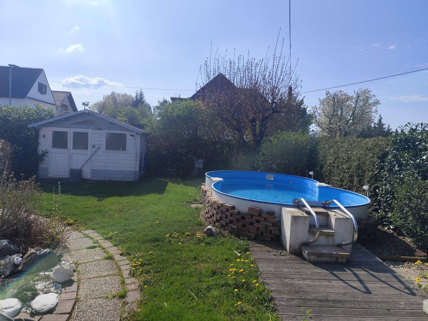 Großer Garten mit oberirdischem Pool, Gartenhaus und einer kleinen Holzterrasse.