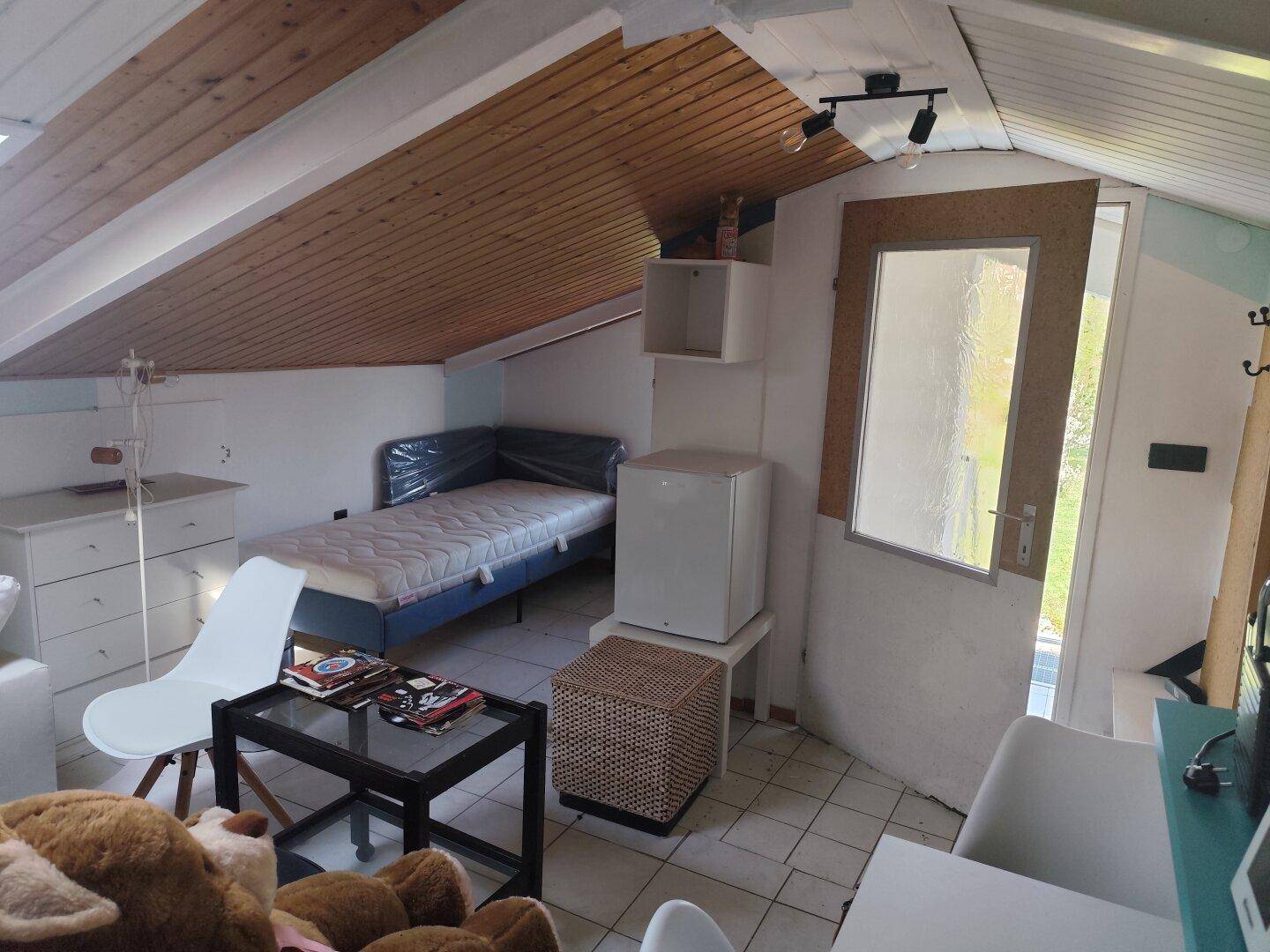 Dachgeschosszimmer mit schräger Holzdecke, Fliesenboden und einem Einzelbett, ideal als Gästezimmer.