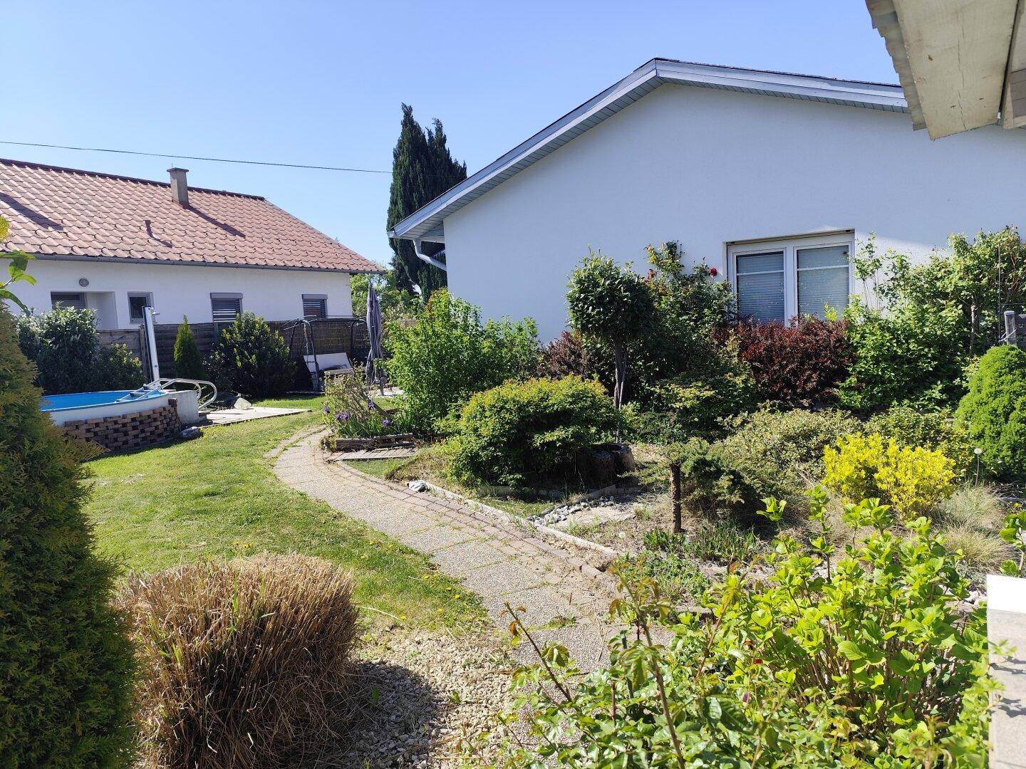 Weitläufiger Gartenbereich mit Pool und der Seitenansicht des Hauses unter strahlendem Sonnenschein.