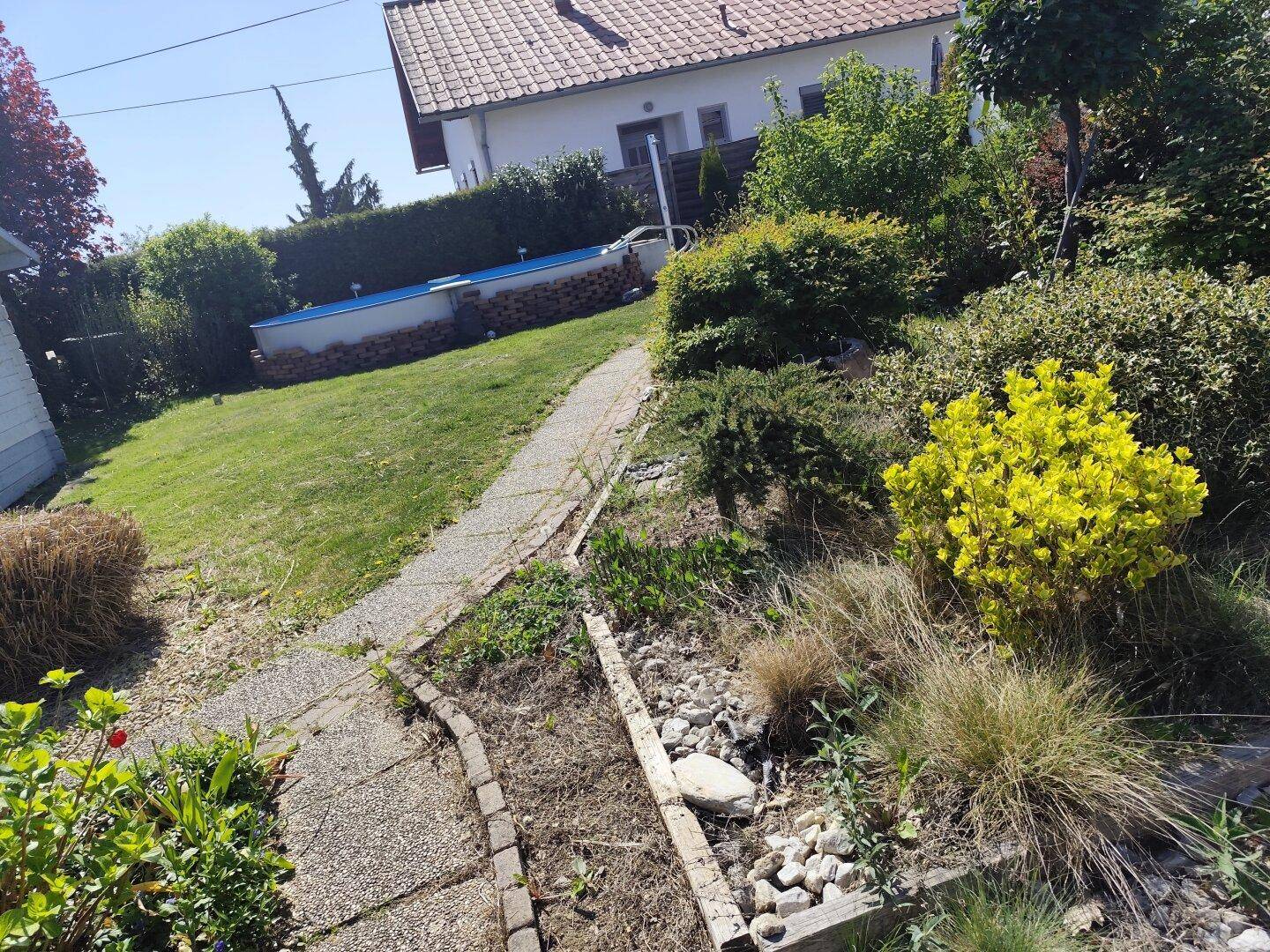 Gartenweg schlängelt sich durch die Bepflanzung, mit Blick auf den Pool in der Ferne.
