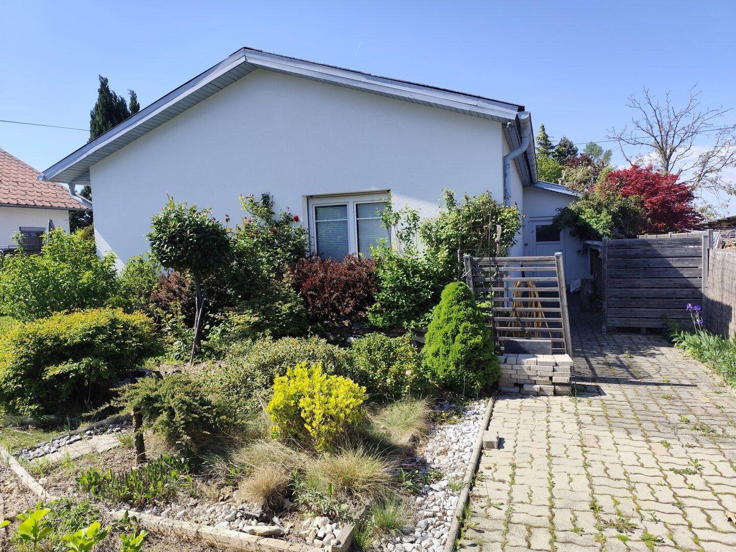 Seitenansicht des Hauses mit gepflastertem Weg und üppiger Bepflanzung im Vorgartenbereich.