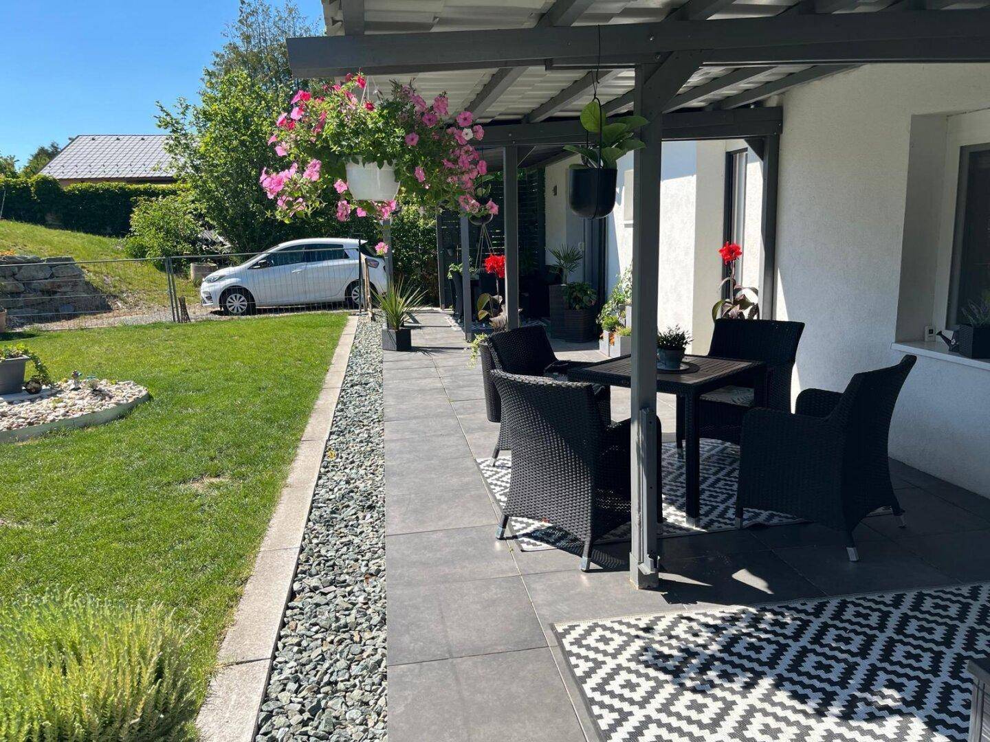 Sonnige Terrasse mit Sitzbereich und Blick auf den grünen Rasen und die umliegende Landschaft.