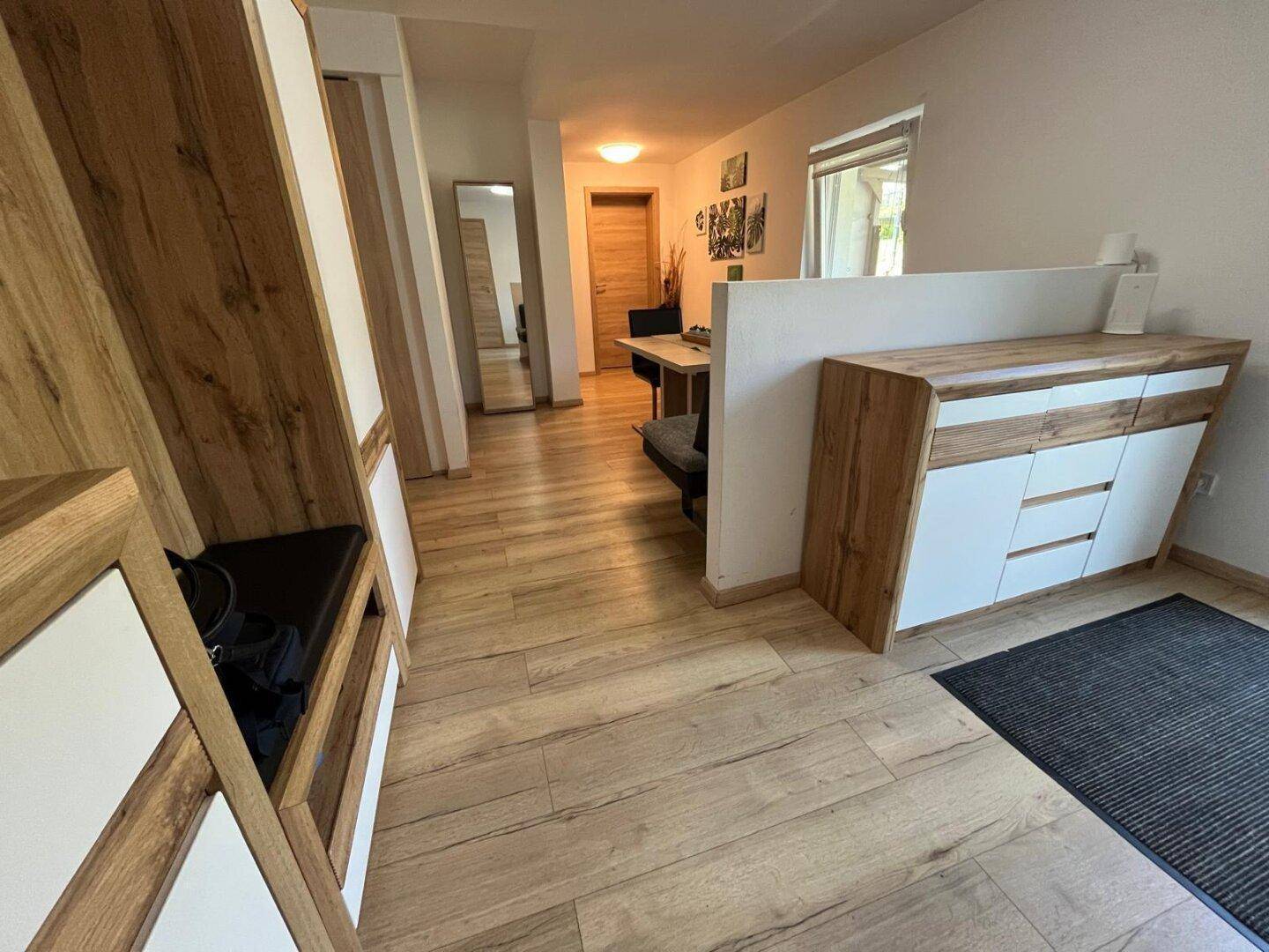 Heller Flur mit Holzoptik-Laminatboden, Garderobe und Kommode, der zu weiteren Räumen führt.