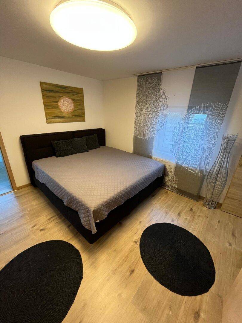 Helles Schlafzimmer mit Doppelbett, dekorativen Vorhängen und Holzboden, das zum Entspannen einlädt.
