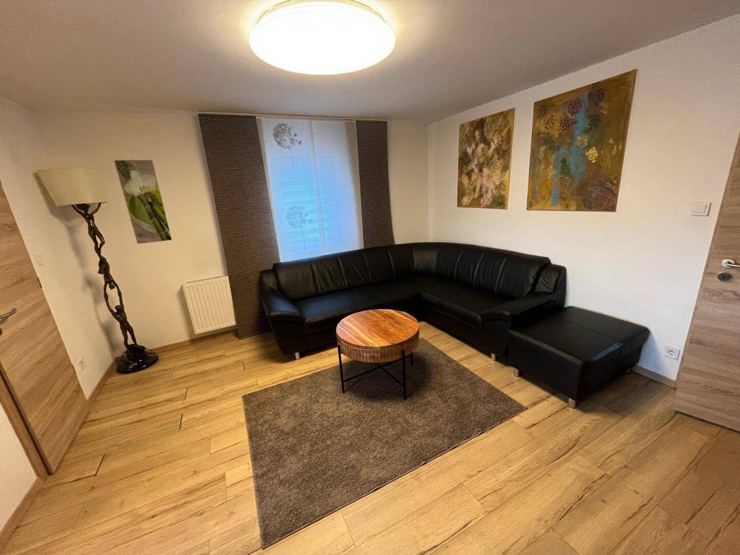 Gemütliches Wohnzimmer mit schwarzem Ledersofa, Holztisch und Kunstwerken an den Wänden.