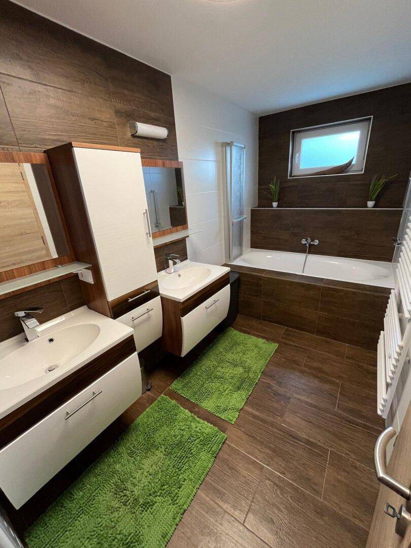 Modernes Badezimmer mit Doppelwaschbecken, Badewanne und braunen Fliesen in Holzoptik.