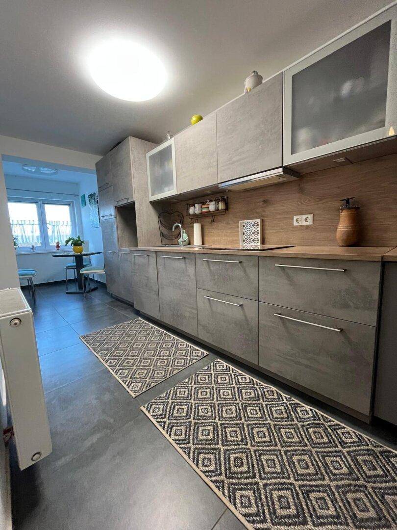 Moderne Küche mit grauen Schränken, Holz-Arbeitsplatte und Essbereich im Hintergrund.