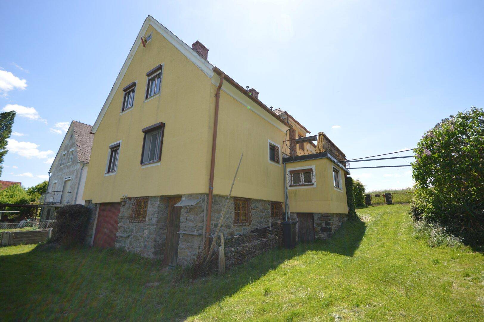 Rückansicht des gelben Hauses mit Steinsockel und Zugang zum Gartenbereich.