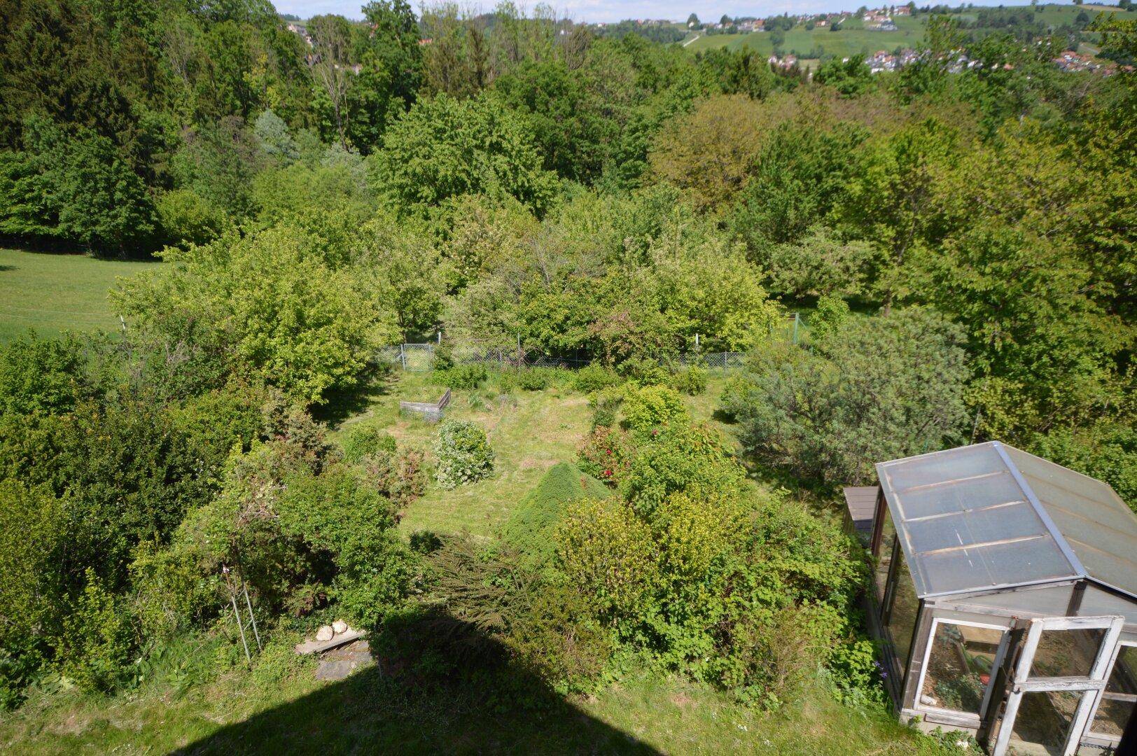 Vogelperspektive auf den weitläufigen Garten mit Gewächshaus und Obstbäumen.