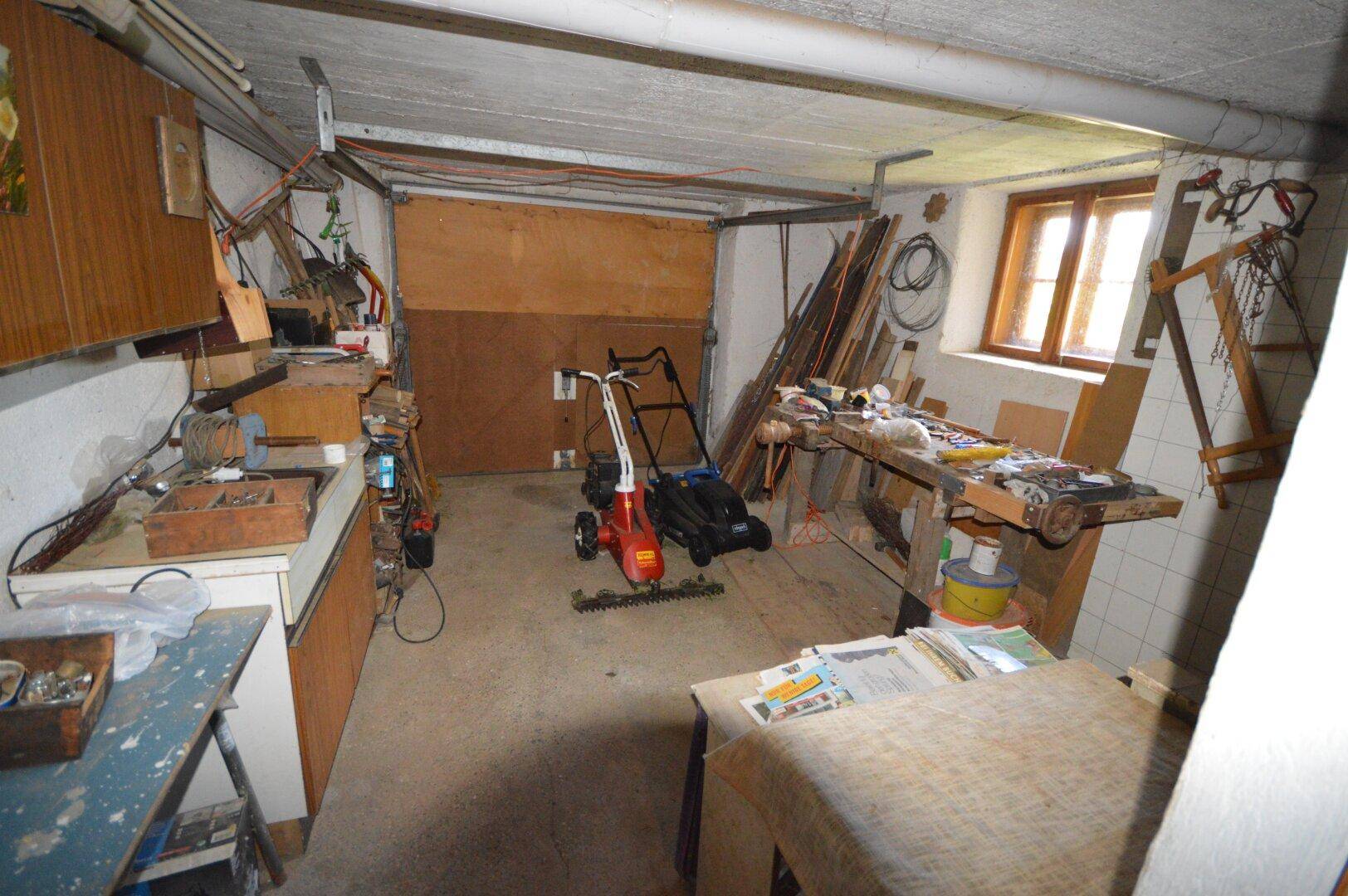 Geräumige Werkstatt im Keller mit Werkbänken, Geräten und Fenster.