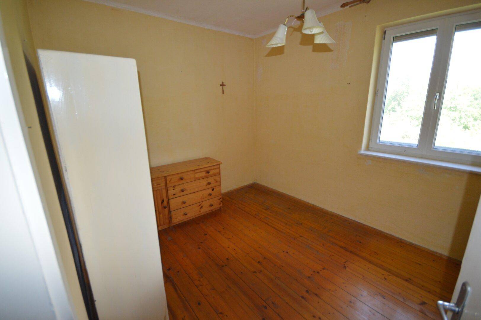 Helles Schlafzimmer mit Holzdielenboden, Kommode und gelben Wänden.