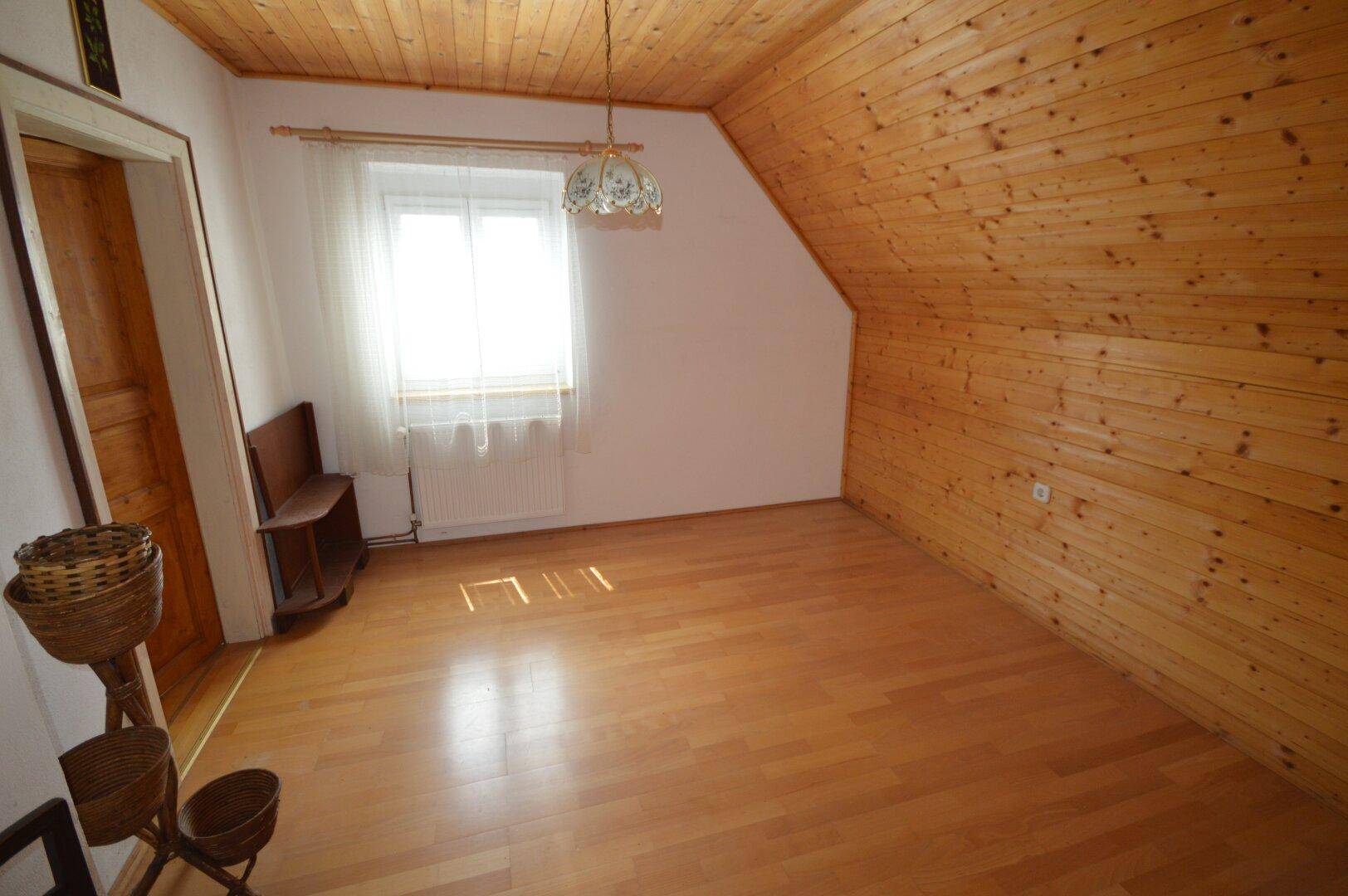 Dachzimmer mit Holzverkleidung, Laminatboden und Fenster mit viel Tageslicht.