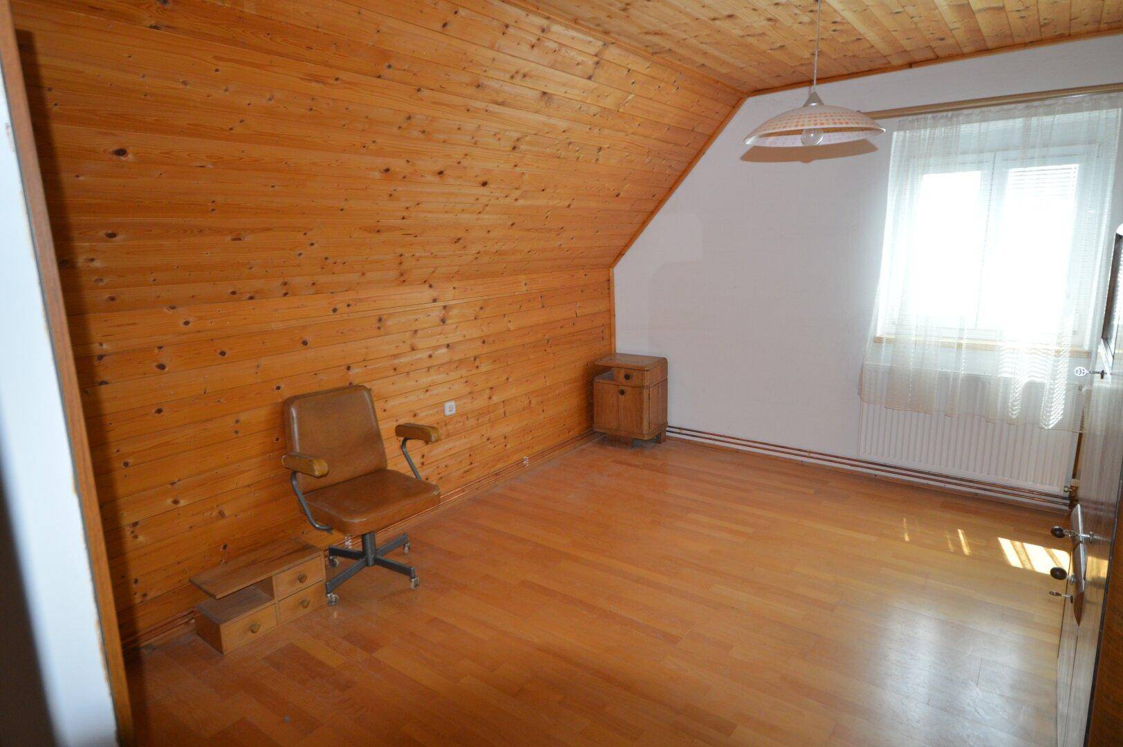 Geräumiges Dachzimmer mit Holzverkleidung, Laminatboden und Bürostuhl.