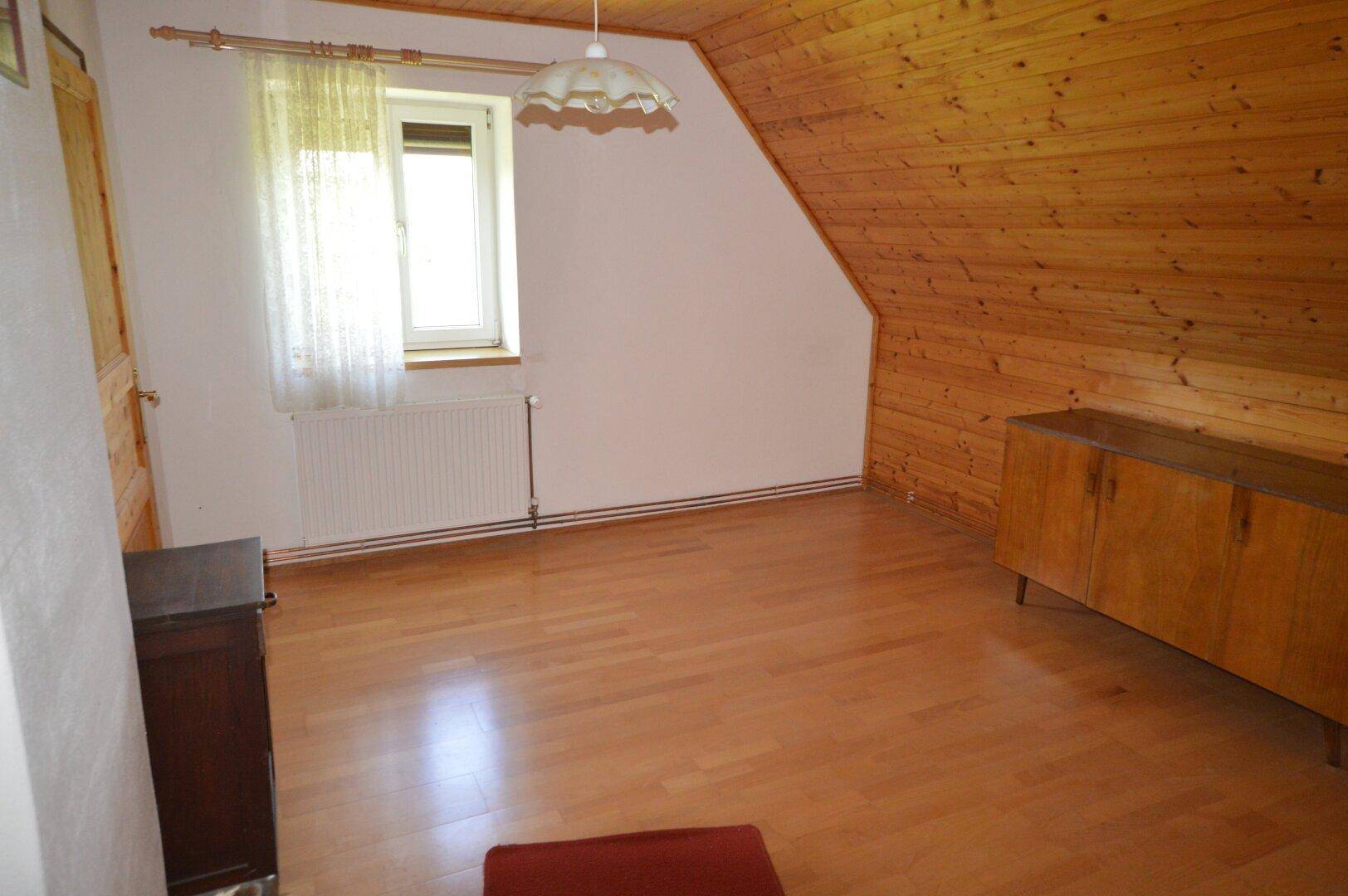 Helles Dachzimmer mit Holzverkleidung, Laminatboden und traditionellen Möbeln.