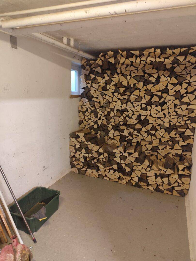 Kellerraum mit einem großen Stapel Brennholz und einem kleinen Fenster für Belüftung.