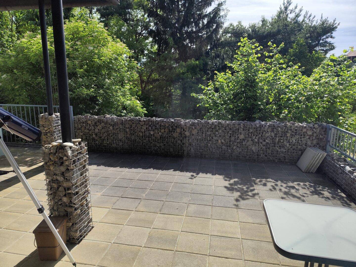 Geräumige Terrasse mit Gabionenmauern und Blick auf die umliegende Natur.