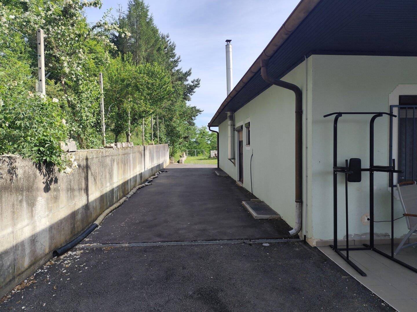 Seitenansicht des Hauses mit asphaltierter Zufahrt und einem Fitnessgerät im Freien.