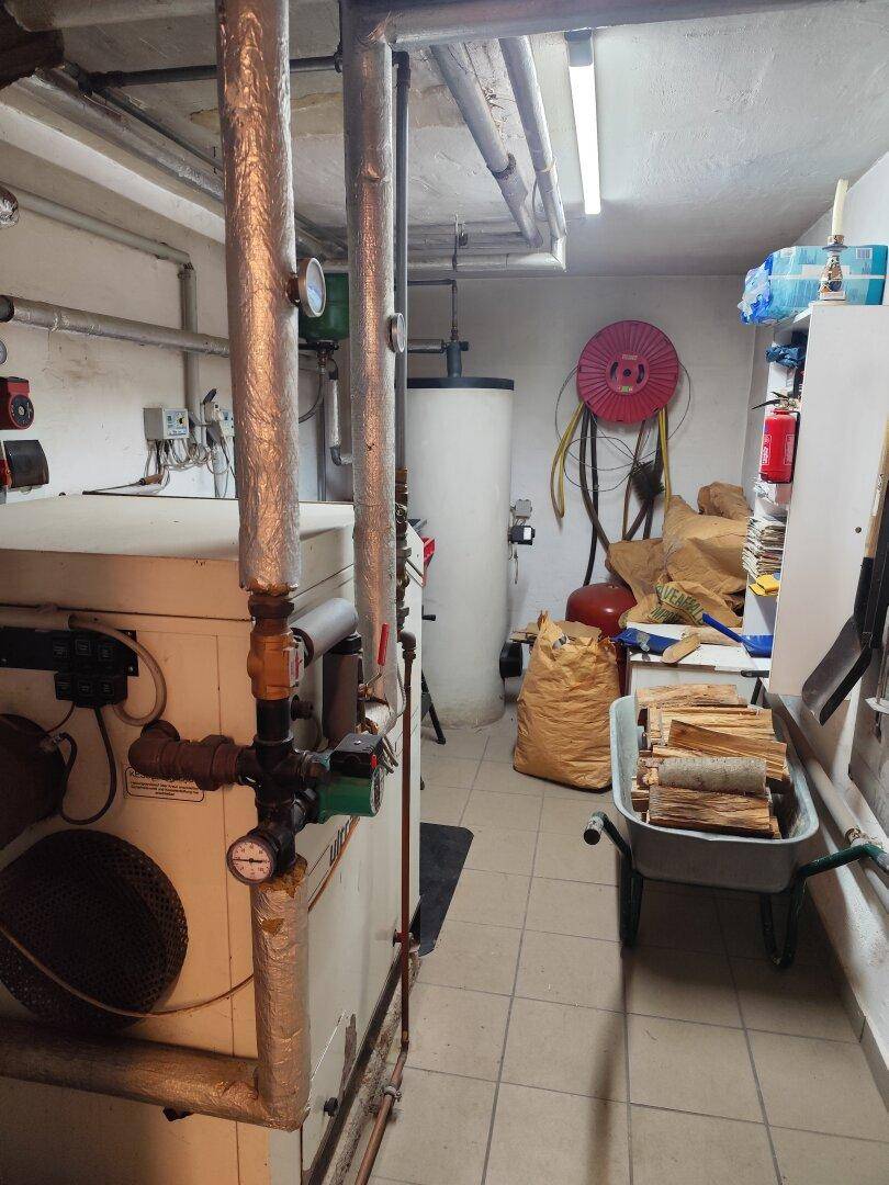 Heizungsraum im Keller mit umfangreicher Installation, Warmwasserspeicher und Lagerfläche.