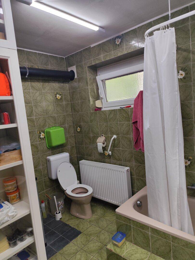 Badezimmer mit grünen Fliesen, Toilette, Badewanne und Fenster für Tageslicht.