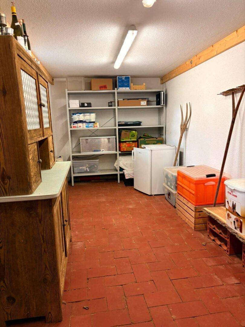 Kellerraum mit Regalen, Kühlschrank und Terrakotta-Fliesenboden für Lagerzwecke.