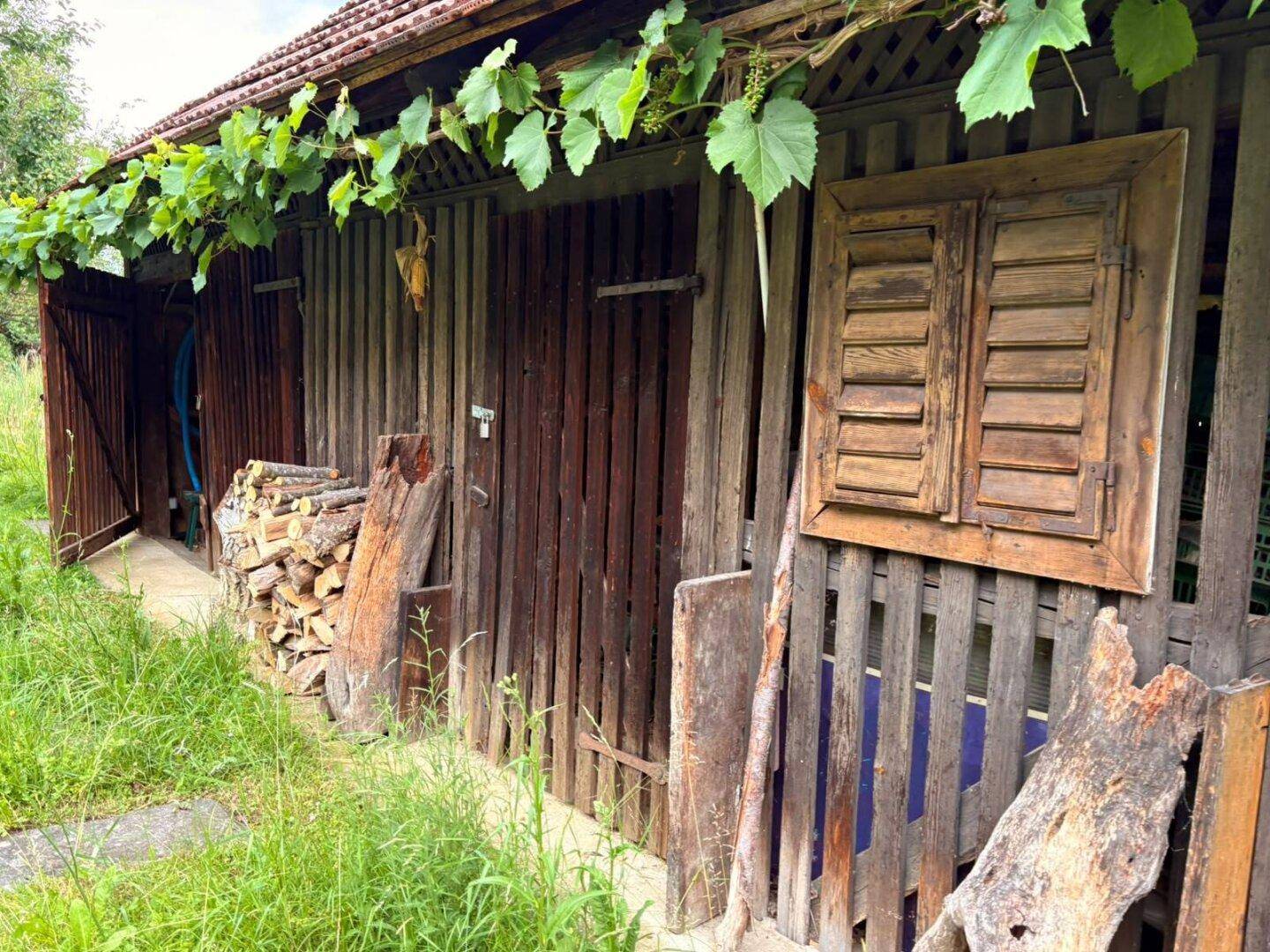 Rustikaler Holzschuppen mit gestapeltem Brennholz und einem kleinen Fenster mit Holzläden.