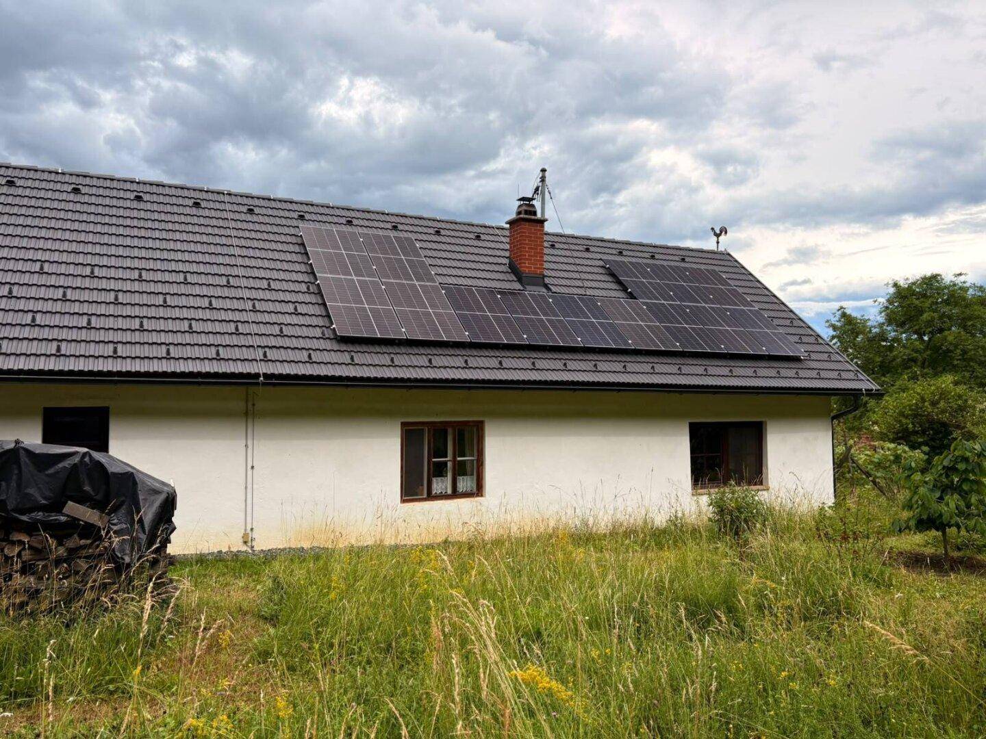 Vorderansicht eines weißen Hauses mit grauem Dach und Solaranlage, umgeben von grüner Wiese.