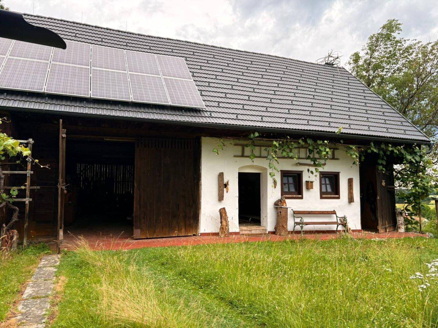 Vorderansicht eines weißen Hauses mit großen Holztoren und Solarmodulen auf dem Dach.