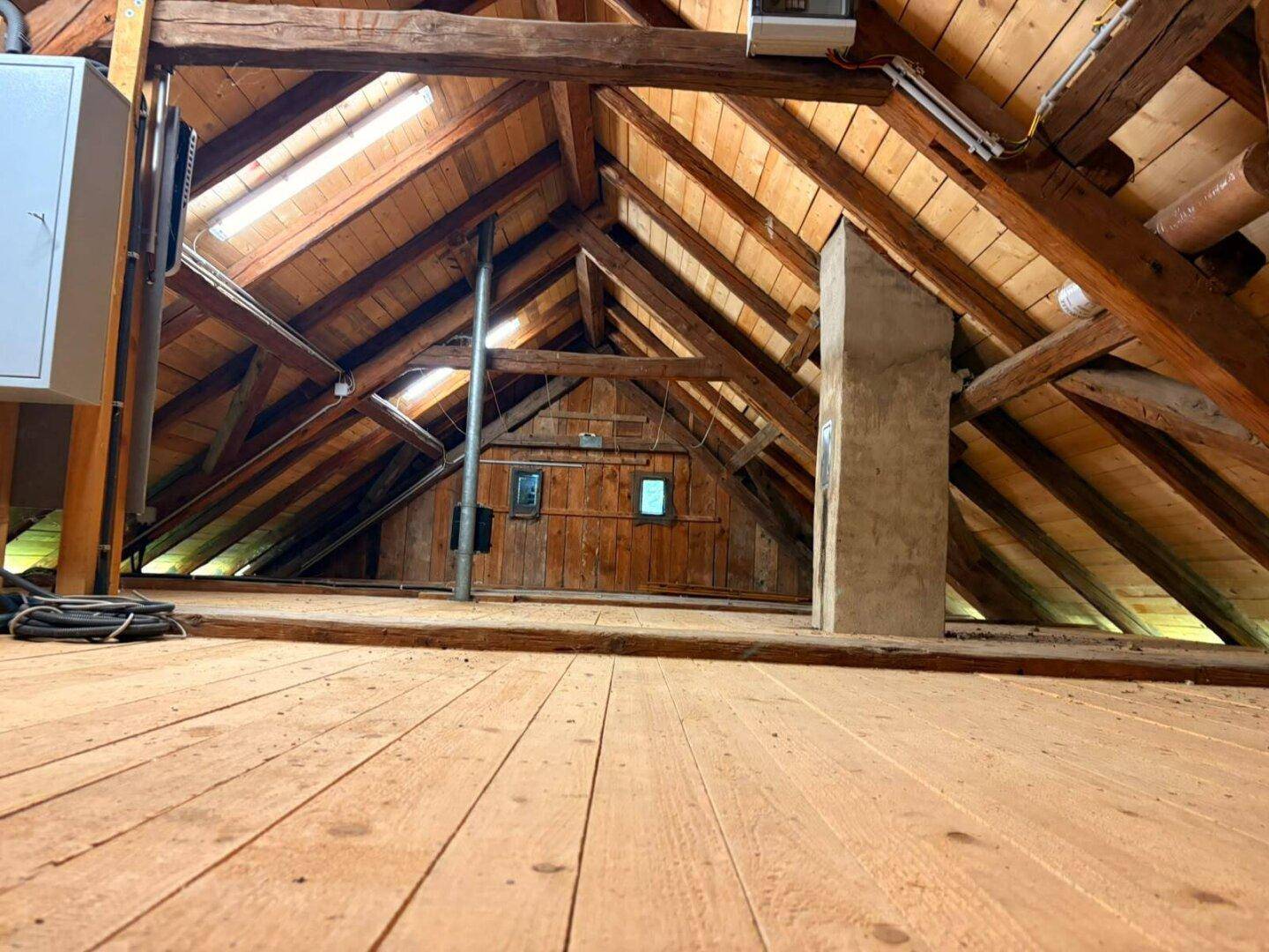 Geräumiger Dachboden mit sichtbaren Holzbalken und Holzboden, ideal als Stauraum.